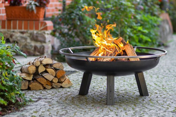 Brasero de jardin Porto 100 cm en acier, posé sur un sol extérieur, avec feu vif et bois brûlant, illustrant l’entretien et la protection contre les intempéries