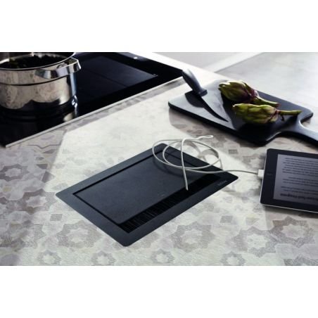 Bloc prise noir encastré sur un îlot de cuisine, plan de travail moderne avec câbles sortant, évier et plaques à proximité visibles