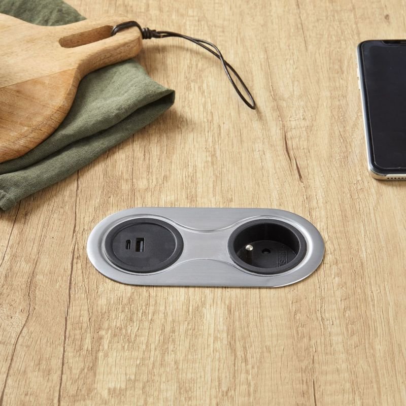 Module en bois clair avec paroso USB-C et prise secteur double sur plan de travail, à côté d’un smartphone.